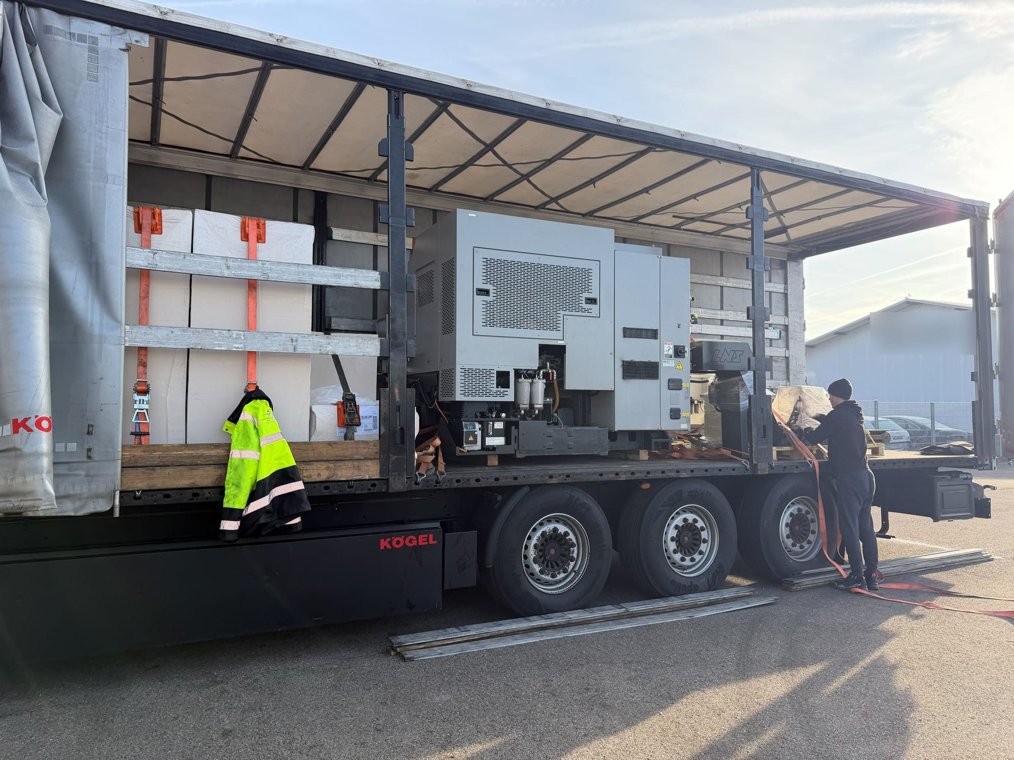 Monteur sichert eine Drehmaschine mit Stangenlader mit Spanngurten auf einem Sattelauflieger