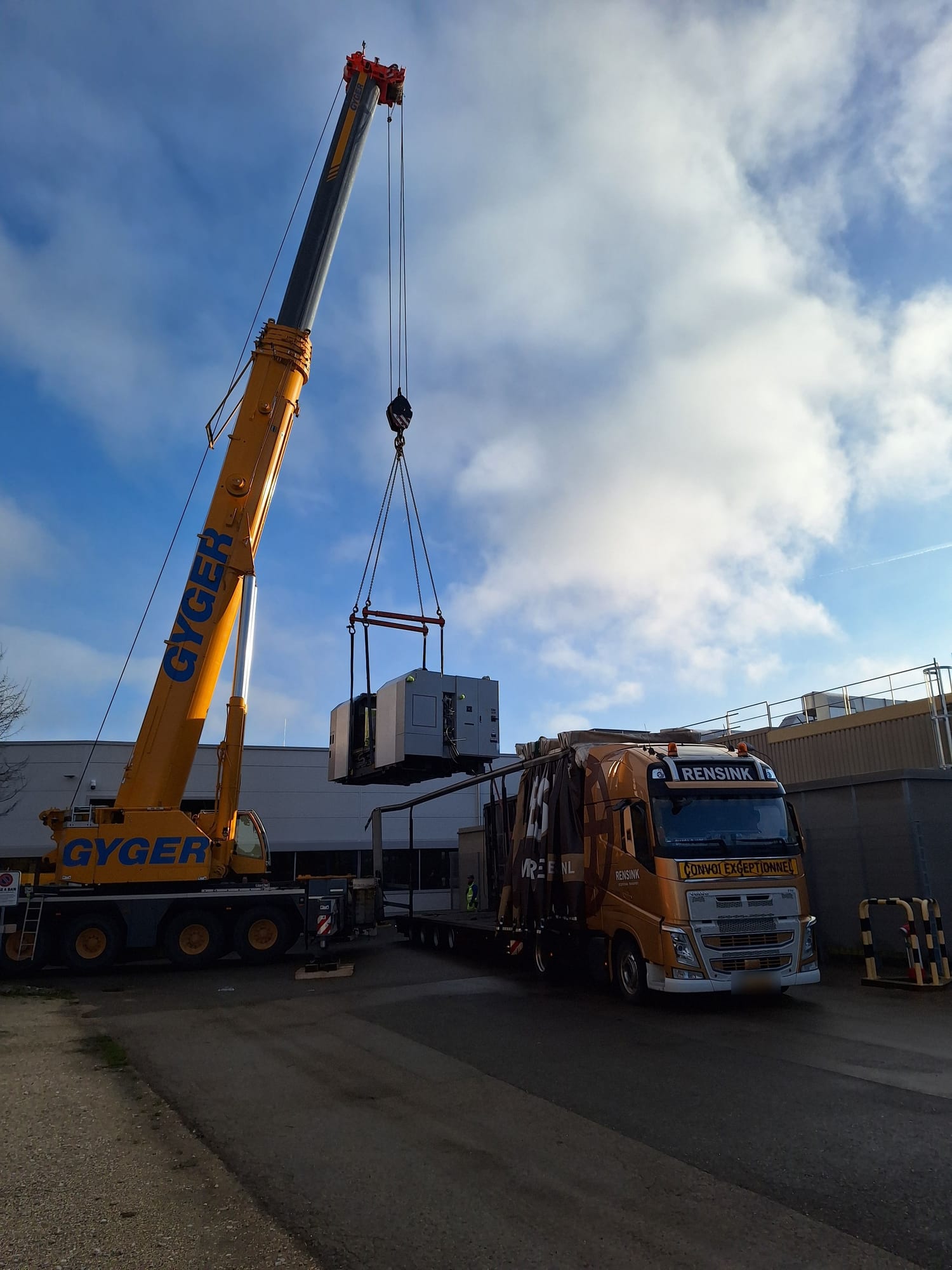 Gelber Mobilkran hebt ein Bearbeitungszentrum über einen Sondertransport-Lkw